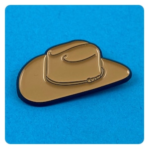 May include: A brown cowboy hat pin with a black outline. The hat has a band around the crown.