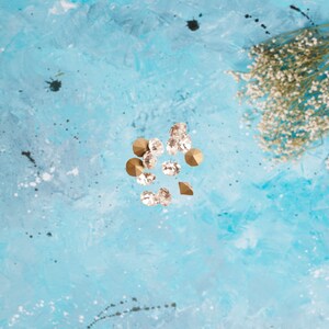 May include: A scattering of clear glass rhinestones and gold-toned metal embellishments on a light blue background.