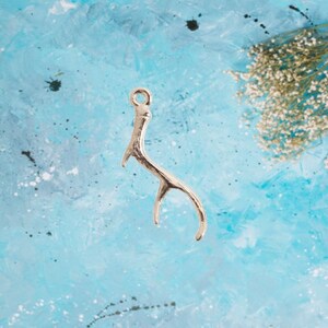May include: Silver antler charm with a loop at the top, against a blue background.