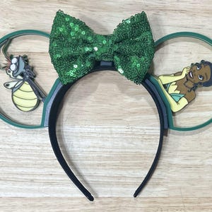 May include: Green and black mouse ears with a green bow, a cartoon frog and a cartoon princess in a green dress.