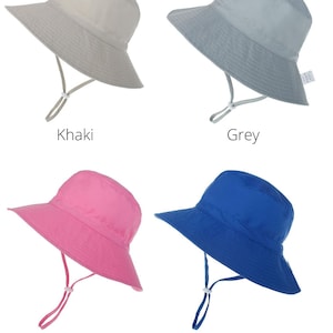 May include: Four sun hats in different colors: khaki, grey, pink, and royal blue. The hats have a wide brim and a chin strap.