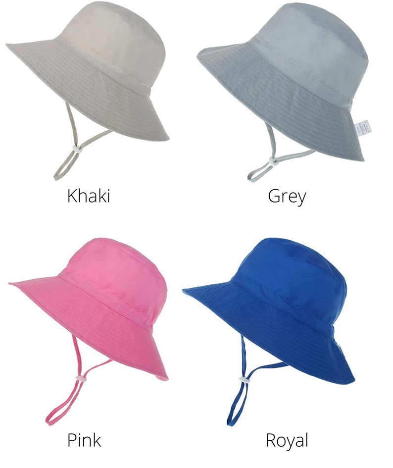May include: Four sun hats in different colors: khaki, grey, pink, and royal blue. The hats have a wide brim and a chin strap.