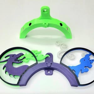May include: A 3D printed wall mount with a green base and purple and blue accents. The mount features a dragon, a unicorn, and clouds.