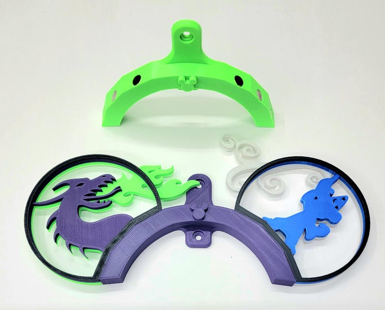 May include: A 3D printed wall mount with a green base and purple and blue accents. The mount features a dragon, a unicorn, and clouds.