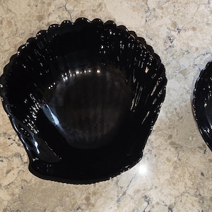 May include: Two black, shell-shaped bowls. The bowls have a glossy finish and a scalloped edge. The bowls are of different sizes, with the larger bowl on the left and the smaller bowl on the right.