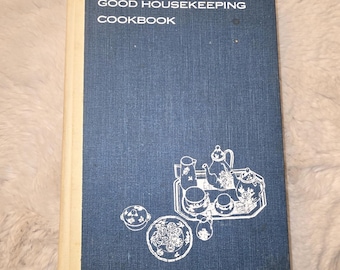 May include: A blue hardcover book titled The Good Housekeeping Cookbook with a white spine. The front cover features white line art illustrations of a tea set on a tray, a small lidded bowl, and a plate of food arranged on the blue fabric texture.