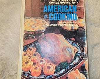 May include: A hardcover cookbook titled The Illustrated Encyclopedia of American Cooking by the editors of Favorite Recipes Press. The cover features a large roasted turkey on a platter surrounded by orange-colored food items and fruit.