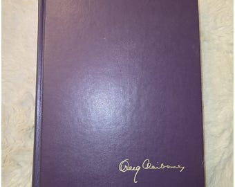 May include: A hardcover book with a solid purple cover. The front cover features the name Craig Claiborne written in gold cursive script in the bottom right corner. The book has a rectangular shape with a visible spine on the left side.