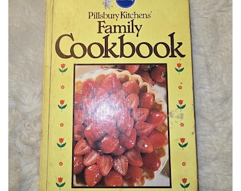 May include: A yellow Pillsbury Kitchens' Family Cookbook with a central photograph of a strawberry tart. The cover features the Pillsbury Doughboy logo, brown text, and a border of small red tulip illustrations on the left and right sides.