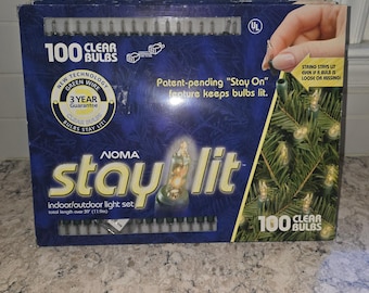 May include: A Noma Stay-Lit indoor/outdoor light set box containing 100 clear bulbs on a green wire. The blue packaging features the text '100 Clear Bulbs', 'Stay-Lit', and 'total length over 39' (11.9m)', highlighting a patent-pending feature.