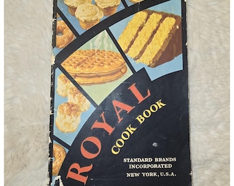 May include: A vintage Royal Cook Book by Standard Brands Incorporated, New York, U.S.A. The cover features a dark blue background with geometric panels displaying illustrations of cupcakes, a slice of cake, a waffle, and biscuits.