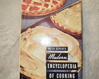 May include: A hardcover cookbook titled Meta Given's Modern Encyclopedia of Cooking, Revised Edition. The cover features a photographic collage of three different pies, including a lattice-top cherry pie and a large meringue-topped pie.