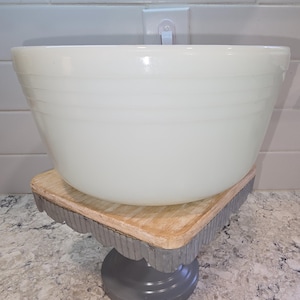 May include: A large, off-white milk glass mixing bowl with a smooth, glossy finish and three horizontal embossed rings around the exterior. The bowl features a wide, circular rim and a tapered base, showcasing a classic, functional kitchen design.
