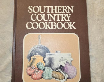May include: A brown hardcover book titled Southern Living Southern Country Cookbook. The cover features a central illustration of a cast iron skillet, a lidded pot, and various vegetables including tomatoes, peppers, corn, and an eggplant.