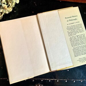 Puede incluir: Un libro cerrado con una cubierta blanca y un lomo amarillo. La contraportada tiene un texto que dice "Pictorial History of Philosophy by  Dagobert D. Runes".
