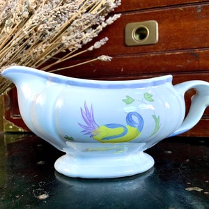 May include: A white porcelain gravy boat with a blue and yellow bird design. The boat has a handle and a base.