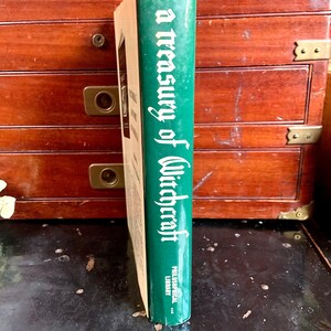 Puede incluir: Un libro de tapa dura verde titulado "A Treasury of Witchcraft" con el logotipo de Philosophical Library en el lomo.
