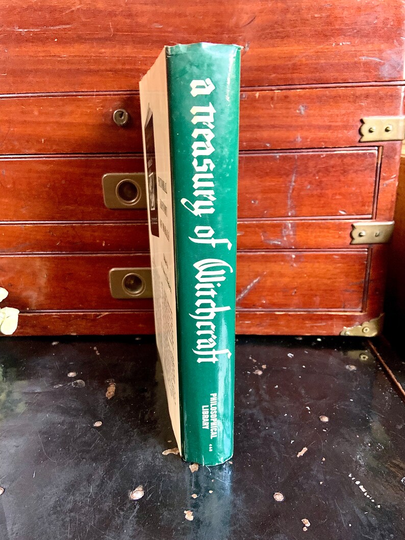 Puede incluir: Un libro de tapa dura verde titulado "A Treasury of Witchcraft" con el logotipo de Philosophical Library en el lomo.