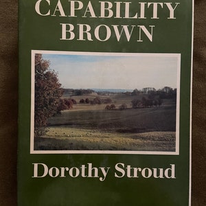 May include: A green book with the title "Capability Brown" and the author "Dorothy Stroud" on the cover. The cover features a photograph of a green field with trees and a distant view of a village.