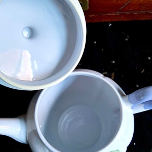 Pu&ograve; includere: Teiera in ceramica bianca con coperchio. La teiera ha un design floreale e un manico. L'interno della teiera &egrave; visibile.