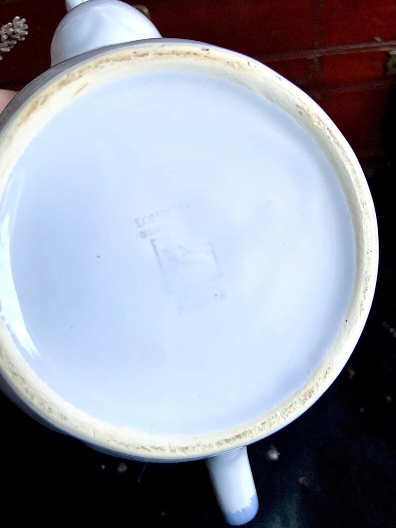 Pu&ograve; includere: Teiera in ceramica bianca con una glassa blu chiaro. Il fondo della teiera ha un piccolo timbro rettangolare sbiadito.