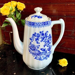 May include: A white porcelain coffee pot with a blue and white floral design. The pot has a gold trim and a lid with a knob.