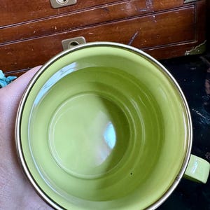 May include: A lime green ceramic mug with a gold rim and handle. The mug's interior is a solid, glossy green. The handle is a matching green. The mug is likely for beverages.