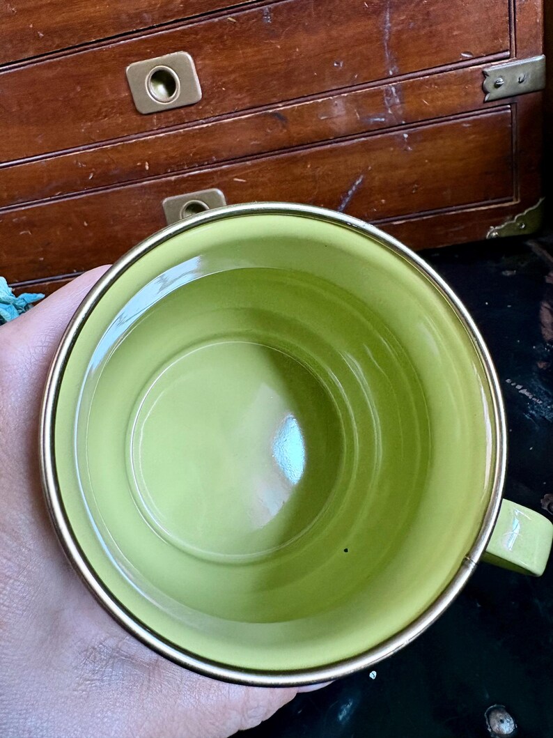 May include: A lime green ceramic mug with a gold rim and handle. The mug's interior is a solid, glossy green. The handle is a matching green. The mug is likely for beverages.