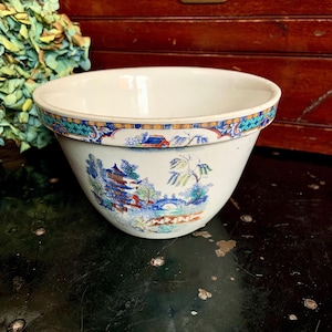 May include: A white ceramic mixing bowl with a blue and yellow floral design. The bowl features a pagoda and a bridge in the design.