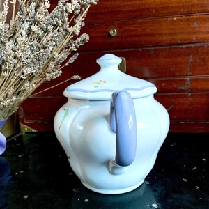 Pu&ograve; includere: Una teiera bianca con un motivo floreale blu e bianco. La teiera ha un manico blu e un coperchio con un pomo.