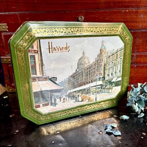 May include: Vintage green and gold decorative tray featuring a detailed illustration of Harrods Knightsbridge. The tray has a rectangular shape with an ornate gold border and the Harrods logo prominently displayed.