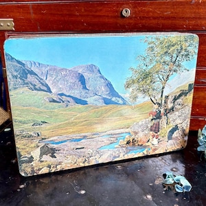 May include: Vintage rectangular tin featuring a scenic landscape with mountains, a river, and a tree. A person in traditional Scottish attire plays bagpipes. The tin has a blue sky and green and brown terrain.