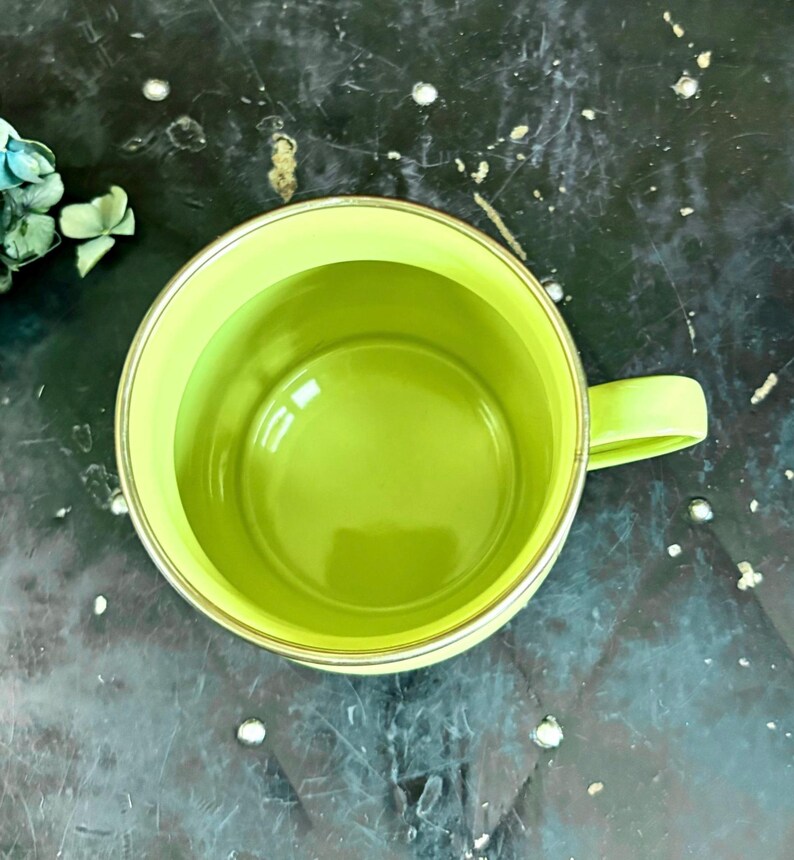 May include: Overhead view of a lime green mug with a matching handle. The interior of the mug is also lime green, and the rim has a thin gold-colored band. The mug is empty and sits on a dark, textured surface.