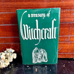Puede incluir: Un libro de tapa dura verde con el t&iacute;tulo "a treasury of Witchcraft" en letras blancas. La portada presenta una ilustraci&oacute;n en blanco y negro de tres figuras de pie alrededor de un caldero.