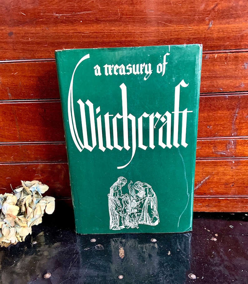 Puede incluir: Un libro de tapa dura verde con el t&iacute;tulo "a treasury of Witchcraft" en letras blancas. La portada presenta una ilustraci&oacute;n en blanco y negro de tres figuras de pie alrededor de un caldero.