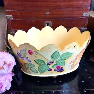 May include: A yellow metal planter with a scalloped rim and painted floral design featuring berries and leaves. The planter has two handles and sits on three small feet.