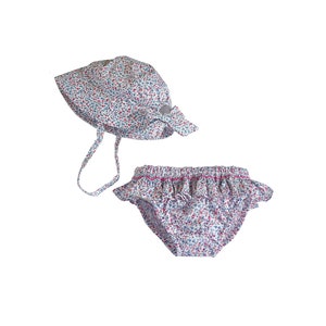 May include: A white swimsuit with a red and blue floral print. The swimsuit has a ruffled bottom and comes with a matching sun hat.
