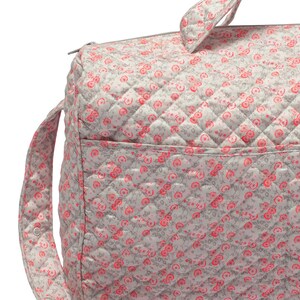 K&ouml;nnte beinhalten: Eine graue gesteppte Wickeltasche mit einem rosa Blumenmuster. Die Tasche hat einen Rei&szlig;verschluss und einen langen Riemen.