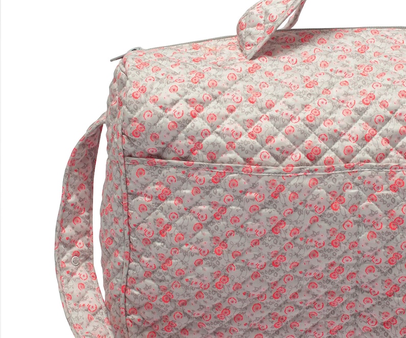 K&ouml;nnte beinhalten: Eine graue gesteppte Wickeltasche mit einem rosa Blumenmuster. Die Tasche hat einen Rei&szlig;verschluss und einen langen Riemen.
