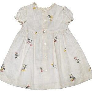 Puede incluir: Un vestido blanco con estampado floral. El vestido tiene mangas cortas y una espalda con botones.
