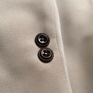 May include: Close-up of a beige blazer with two brown buttons on the sleeve.