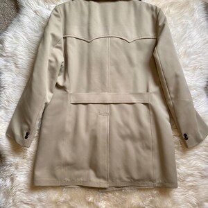 May include: A beige trench coat with a black faux fur collar. The coat has a single breasted closure and a belt in the back.