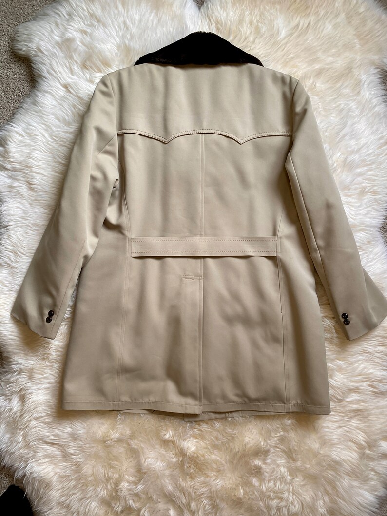 May include: A beige trench coat with a black faux fur collar. The coat has a single breasted closure and a belt in the back.