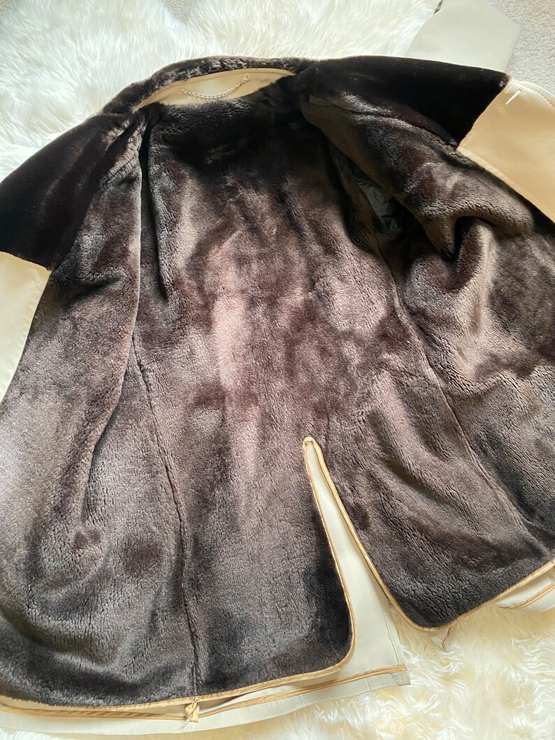 May include: A cream-colored faux fur jacket with a brown faux fur lining. The jacket is unzipped and the lining is visible.