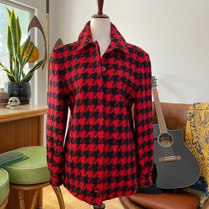 Könnte beinhalten: Eine rot-schwarze Hahnentritt-Jacke mit Knopfleiste. Die Jacke befindet sich auf einem Mannequin und hat lange Ärmel.