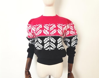 May include: A vintage sweater with a bold color block design. The top is bright pink, transitioning to a white and black patterned section, and ending with a black bottom and sleeves. The sweater is displayed on a mannequin.