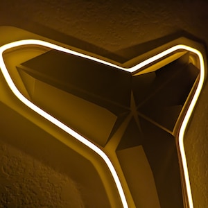 May include: A geometric, abstract design with a star-like shape, illuminated by a warm, yellow neon light. The design is set against a textured, dark background, creating a striking contrast. The light outlines the edges of the structure.