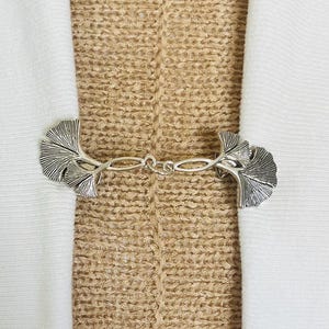 May include: Silver tone ginkgo leaf cardigan clasp. The clasp is made of two ginkgo leaves connected by a chain.