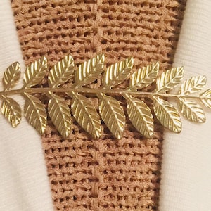 May include: A gold-colored leaf branch brooch with a delicate design. The brooch is made of metal and has a detailed, intricate pattern.