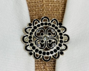 May include: A silver and black decorative brooch with a circular design and clear rhinestones.